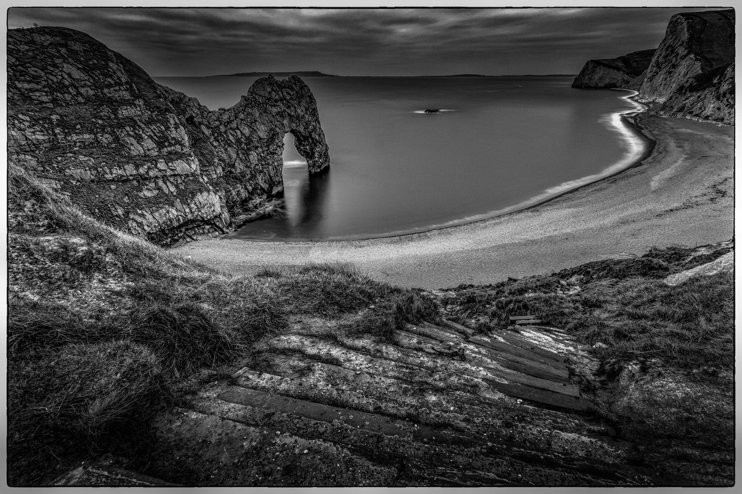 Black and white photograph of Durdle Door limestone arch on the Jurassic Coast in Dorset, England, with dramatic coastal atmosphere.