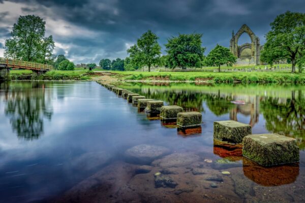 Stepping stones crossing a shallow river in the English countryside surrounded by greenery