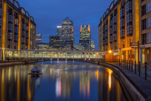 Canary Wharf skyline in London, England, during blue hour with illuminated skyscrapers reflected on the water