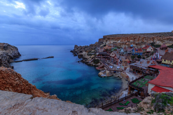 Popeye Village in Malta during blue hour on a cloudy day, with colourful wooden houses along the coastline