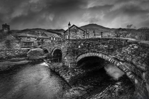 Black and white photograph of a historic stone bridge in Wales over a calm river